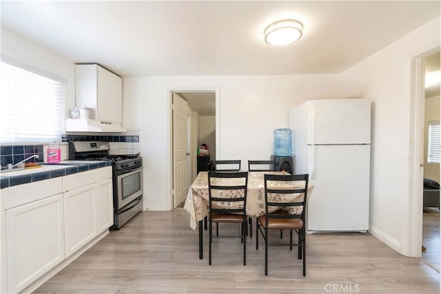 285 W 9th St, San Pedro, CA 90731 - kitchen with freestanding refrigerator, gas stove, under cabinet range hood, tile countertops, and white cabinets