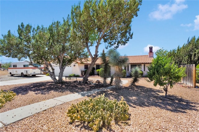 7390 Chase Ave, Hesperia, CA 92345 - view of property hidden behind natural elements featuring a tiled roof, a chimney, concrete driveway, stucco siding, and a garage