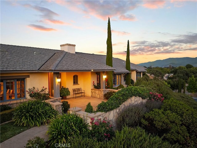 1559 Rolling Hills Rd, Santa Ynez, CA 93460 - back of house at dusk featuring stucco siding, a chimney, a mountain view, and covered porch