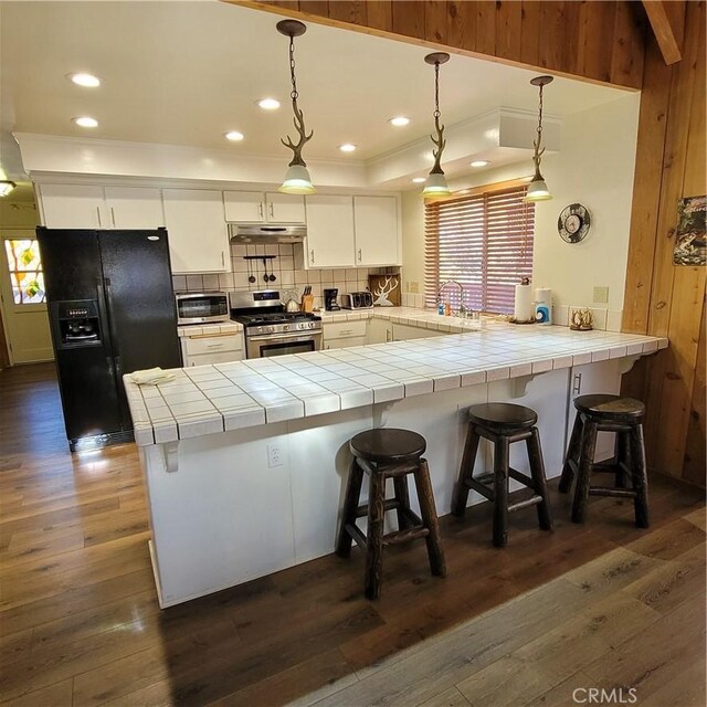 1126 Aleutian Dr, Lake Arrowhead, CA 92352 - kitchen featuring stainless steel gas range oven, black fridge with ice dispenser, under cabinet range hood, a peninsula, and tile counters
