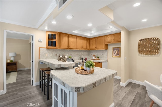 3020 Associated Rd Unit 110, Fullerton, CA 92835 - kitchen with tile countertops, light wood-style flooring, decorative backsplash, glass insert cabinets, and crown molding