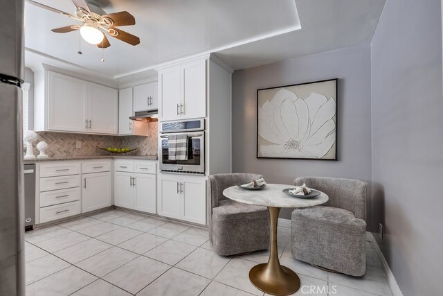 1354 Shadow Ln Unit 102, Fullerton, CA 92831 - kitchen with oven, decorative backsplash, under cabinet range hood, a ceiling fan, and white cabinetry