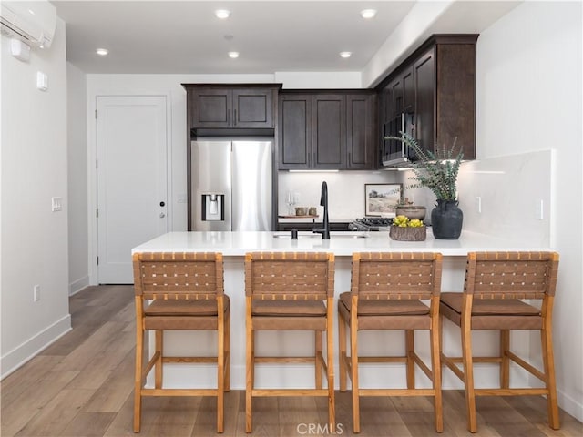 402 W Grand Ave Unit 104, Grover Beach, CA 93433 - kitchen with stainless steel appliances, a peninsula, light wood-style flooring, dark brown cabinets, and an AC wall unit