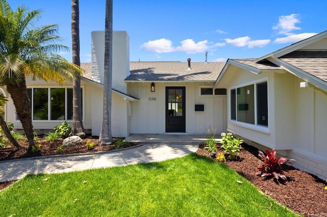 11741 Foster Rd, Los Alamitos, CA 90720 - view of front facade featuring roof with shingles, board and batten siding, a chimney, and a front lawn