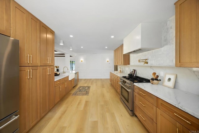 11741 Foster Rd, Los Alamitos, CA 90720 - kitchen featuring appliances with stainless steel finishes, light wood-type flooring, custom exhaust hood, brown cabinetry, and light stone countertops