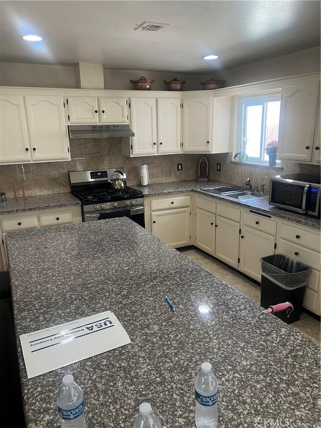 26832 6th St, Highland, CA 92346 - kitchen featuring stainless steel appliances, under cabinet range hood, backsplash, white cabinetry, and dark stone counters