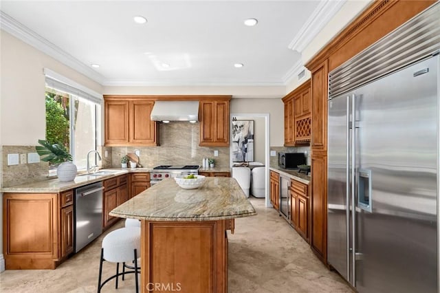 61 Clermont, Newport Coast, CA 92657 - kitchen with stainless steel appliances, wall chimney range hood, a kitchen breakfast bar, light stone countertops, and tasteful backsplash