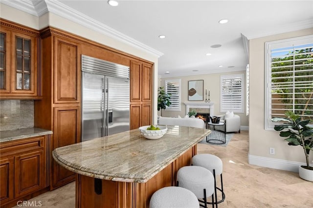 61 Clermont, Newport Coast, CA 92657 - kitchen featuring stainless steel built in fridge, brown cabinetry, recessed lighting, a warm lit fireplace, and a center island