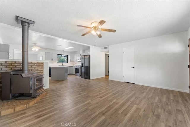 21999 Riverside Ave, Red Bluff, CA 96080 - unfurnished living room featuring a ceiling fan, light wood finished floors, a wood stove, and a textured ceiling
