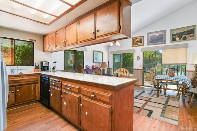 3096 Coral Tree Ln, Fallbrook, CA 92028 - kitchen with a peninsula, brown cabinetry, lofted ceiling, black dishwasher, and light wood-style floors