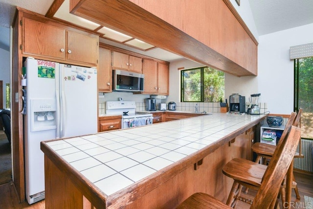 3096 Coral Tree Ln, Fallbrook, CA 92028 - kitchen with white appliances, tile counters, a peninsula, and wood finished floors