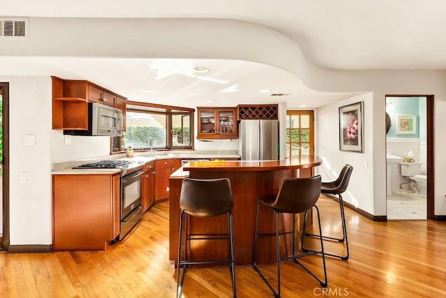 34283 Via Lopez, Dana Point, CA 92624 - kitchen featuring appliances with stainless steel finishes, a kitchen bar, light wood-type flooring, glass insert cabinets, and open shelves
