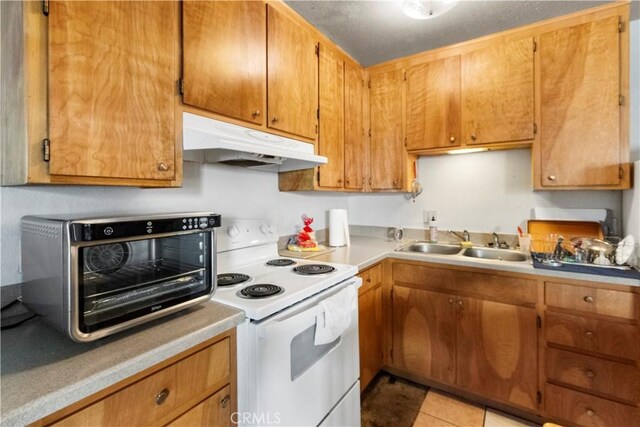 351 W 19th St, Merced, CA 95340 - kitchen with white electric stove, under cabinet range hood, light countertops, light tile patterned floors, and brown cabinetry