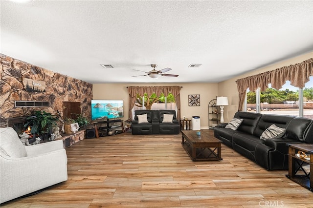 19082 Tecumseh Rd, Apple Valley, CA 92307 - living room featuring light wood finished floors, a textured ceiling, a ceiling fan, and a stone fireplace