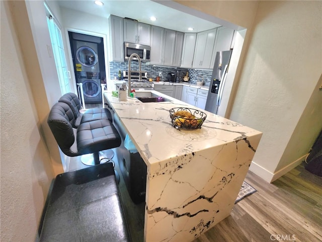 8626 Laurel Canyon Blvd, Sun Valley, CA 91352 - kitchen with stacked washer / dryer, appliances with stainless steel finishes, a textured wall, tasteful backsplash, and wood finished floors