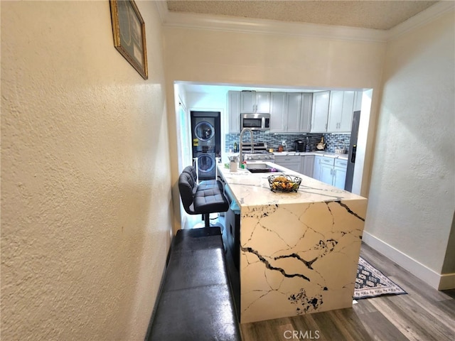 8626 Laurel Canyon Blvd, Sun Valley, CA 91352 - kitchen featuring stainless steel microwave, stacked washer and clothes dryer, crown molding, wood finished floors, and tasteful backsplash