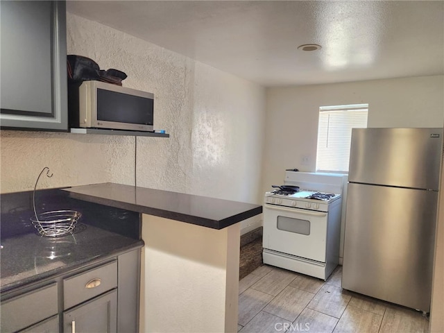 8626 Laurel Canyon Blvd, Sun Valley, CA 91352 - kitchen with freestanding refrigerator, white gas stove, dark countertops, a textured wall, and wood finish floors