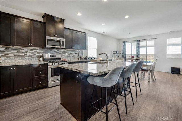1246 Venice Ave, Mentone, CA 92359 - kitchen with appliances with stainless steel finishes, light wood-style floors, light stone countertops, a center island with sink, and a breakfast bar area