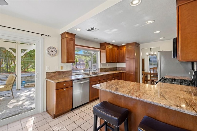 28610 Cloverleaf Pl, Castaic, CA 91384 - kitchen featuring appliances with stainless steel finishes, a peninsula, brown cabinets, a chandelier, and light stone countertops