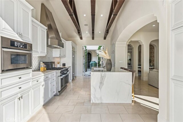 3 Coral Cay, Newport Coast, CA 92657 - kitchen with stainless steel appliances, arched walkways, beamed ceiling, decorative backsplash, and wall chimney exhaust hood