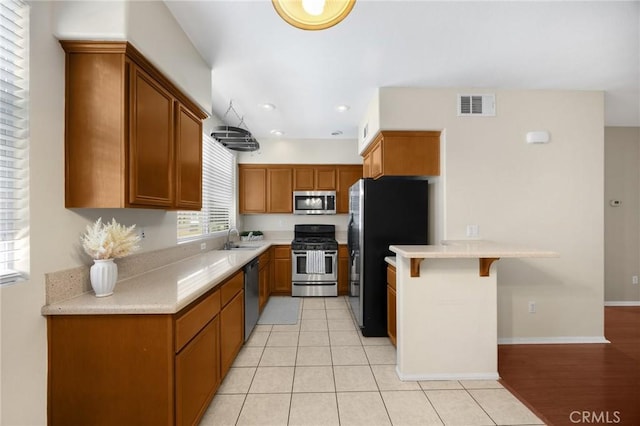 1565 Ledgestone Ln, Pomona, CA 91767 - kitchen featuring stainless steel appliances, a peninsula, brown cabinetry, light countertops, and a breakfast bar area