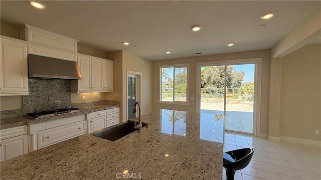 1167 Tesoro Pl, Vista, CA 92081 - kitchen featuring wall chimney exhaust hood, stainless steel gas stovetop, tasteful backsplash, light stone counters, and white cabinets