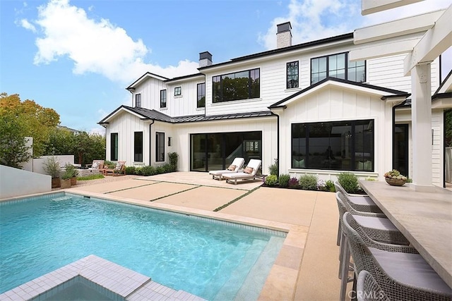2001 Port Ramsgate Pl, Newport Beach, CA 92660 - rear view of house featuring a chimney, board and batten siding, a standing seam roof, a patio area, and a metal roof