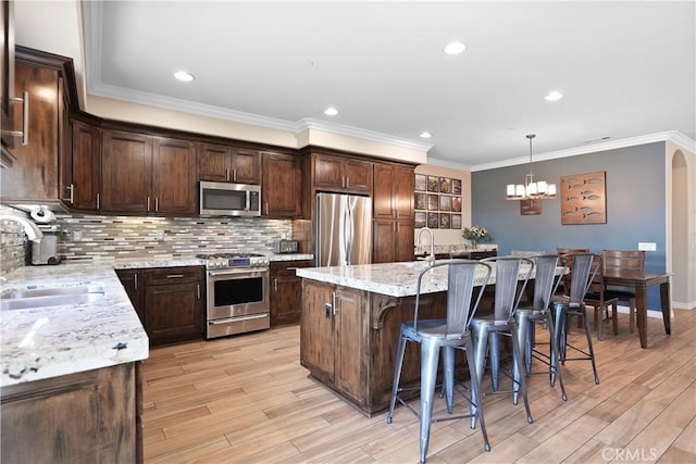 1018 W 15th St, Upland, CA 91786 - kitchen with appliances with stainless steel finishes, light wood-style flooring, a breakfast bar area, a kitchen island with sink, and dark brown cabinets