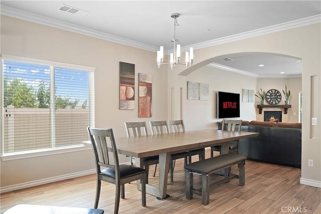 1018 W 15th St, Upland, CA 91786 - dining room with light wood finished floors, a lit fireplace, a chandelier, arched walkways, and crown molding