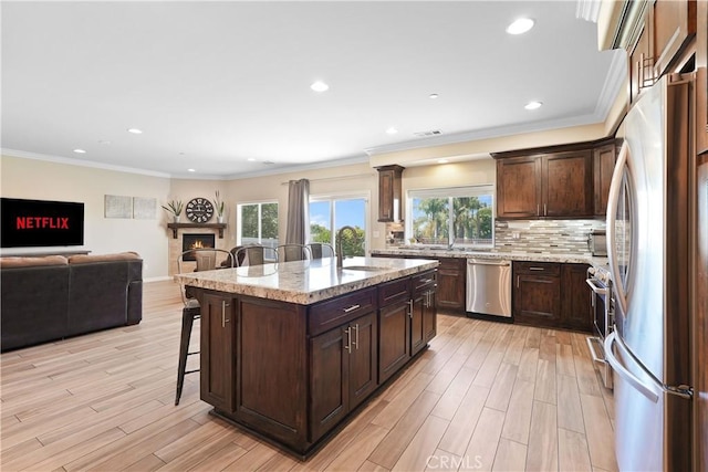 1018 W 15th St, Upland, CA 91786 - kitchen with appliances with stainless steel finishes, a kitchen breakfast bar, a warm lit fireplace, open floor plan, and a center island with sink