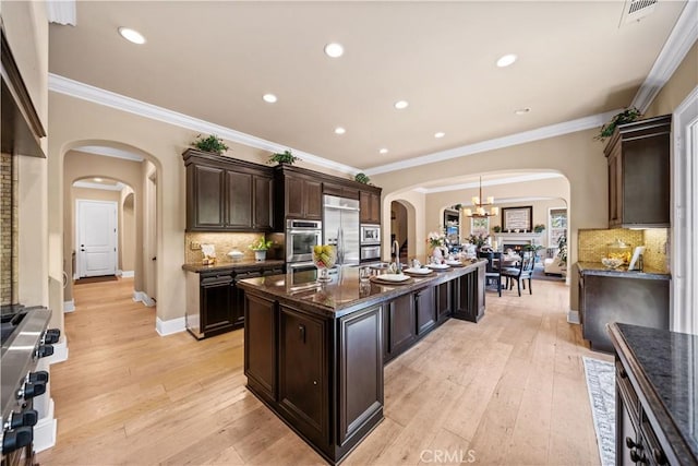 19668 Three Oaks Ln, Walnut, CA 91789 - kitchen featuring arched walkways, stainless steel appliances, a kitchen island with sink, dark stone counters, and dark brown cabinets