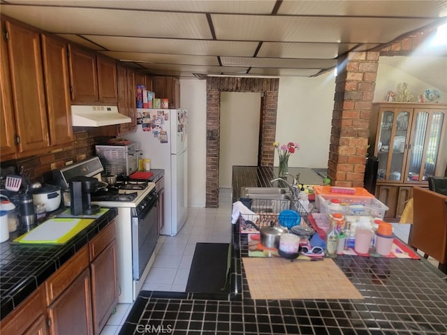 8502 Borson St, Downey, CA 90242 - kitchen with tile countertops, white range with gas stovetop, under cabinet range hood, light tile patterned floors, and brown cabinetry