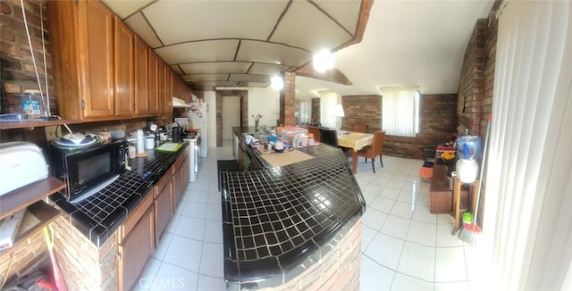 8502 Borson St, Downey, CA 90242 - kitchen featuring brown cabinets, brick wall, black microwave, light tile patterned flooring, and under cabinet range hood