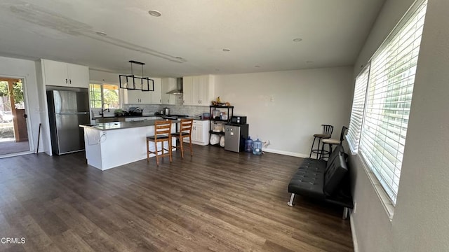 325 Del Sur Way, Oxnard, CA 93033 - kitchen with freestanding refrigerator, wall chimney range hood, white cabinetry, decorative backsplash, and a breakfast bar area