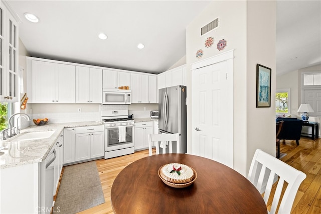 23974 Via Astuto, Murrieta, CA 92562 - kitchen featuring white appliances, vaulted ceiling, healthy amount of natural light, light wood-style floors, and white cabinetry