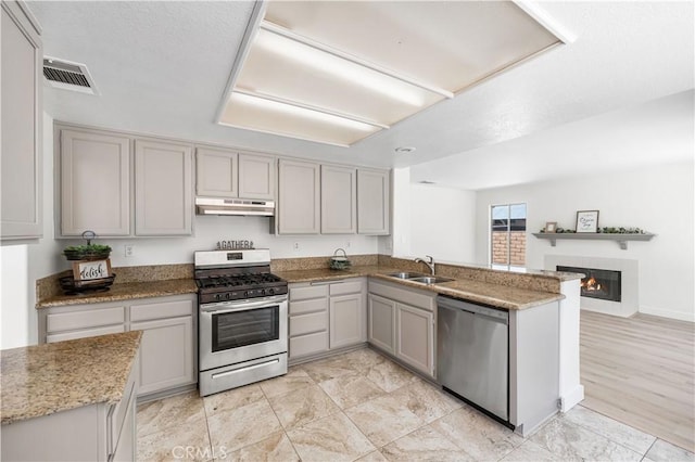 39524 Hawthorne St, Palmdale, CA 93551 - kitchen with stainless steel appliances, gray cabinets, under cabinet range hood, a glass covered fireplace, and a peninsula