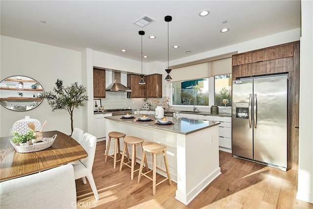 1050 N Joels Pl, Los Angeles, CA 90012 - kitchen with stainless steel refrigerator with ice dispenser, wall chimney exhaust hood, light wood-style flooring, a breakfast bar, and tasteful backsplash