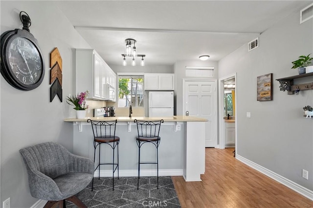 20191 Cape Coral Ln Unit 3-206, Huntington Beach, CA 92646 - kitchen with white appliances, a peninsula, a kitchen bar, white cabinetry, and wood finished floors