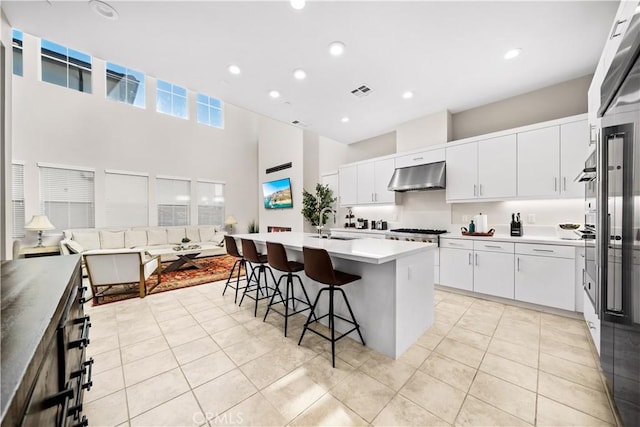 151 Fremont, Lake Forest, CA 92630 - kitchen with under cabinet range hood, a towering ceiling, a kitchen island with sink, a breakfast bar, and light countertops