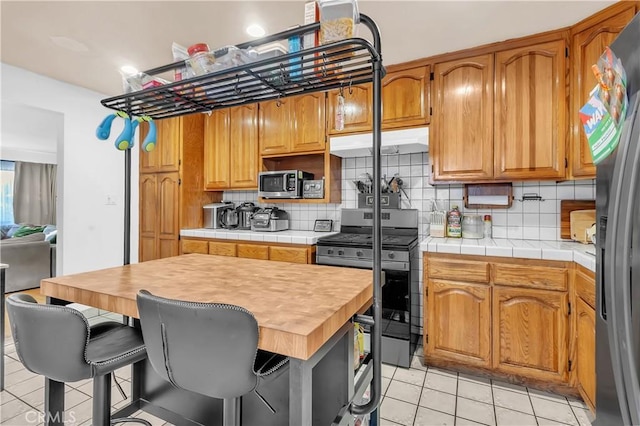 7708 Birchleaf Ave, Pico Rivera, CA 90660 - kitchen with stainless steel appliances, light tile patterned flooring, under cabinet range hood, decorative backsplash, and brown cabinetry