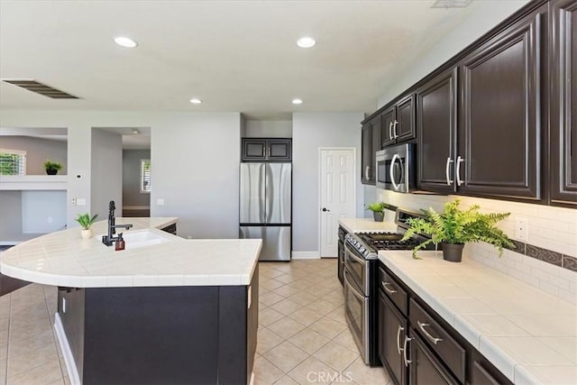 6701 Whitewater St, Eastvale, CA 91752 - kitchen featuring appliances with stainless steel finishes, light tile patterned floors, tasteful backsplash, tile countertops, and an island with sink