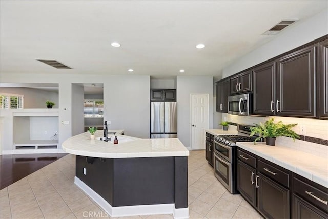 6701 Whitewater St, Eastvale, CA 91752 - kitchen with appliances with stainless steel finishes, light tile patterned floors, decorative backsplash, an island with sink, and tile countertops