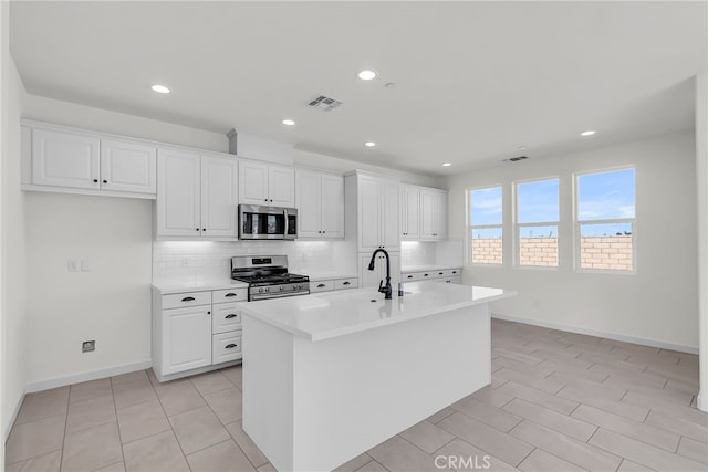 7444 Desert Sky Dr, Yucca Valley, CA 92284 - kitchen featuring stainless steel appliances, decorative backsplash, an island with sink, white cabinets, and light countertops