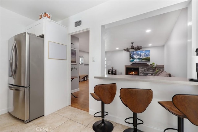 13708 El Espejo Rd, La Mirada, CA 90638 - kitchen with freestanding refrigerator, a kitchen bar, a lit fireplace, light tile patterned floors, and white cabinetry