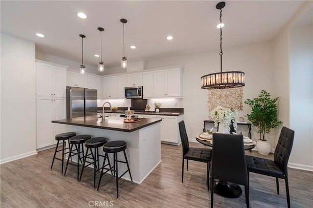 18 Jaripol Cir, Rancho Mission Viejo, CA 92694 - kitchen with appliances with stainless steel finishes, dark countertops, a center island with sink, wood finished floors, and white cabinets