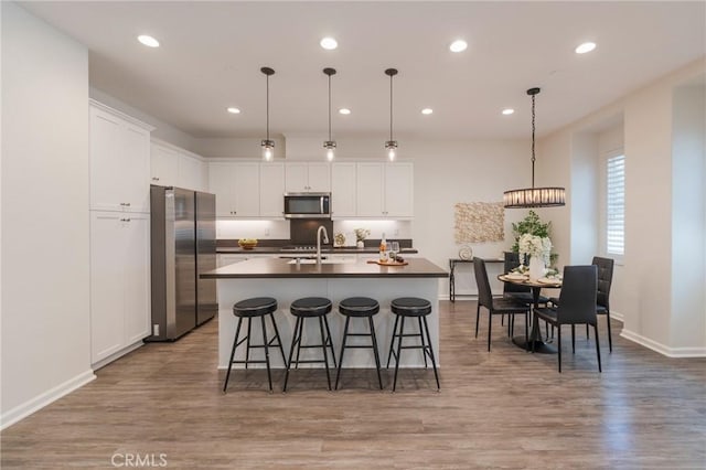 18 Jaripol Cir, Rancho Mission Viejo, CA 92694 - kitchen with appliances with stainless steel finishes, dark countertops, an island with sink, white cabinetry, and a kitchen bar