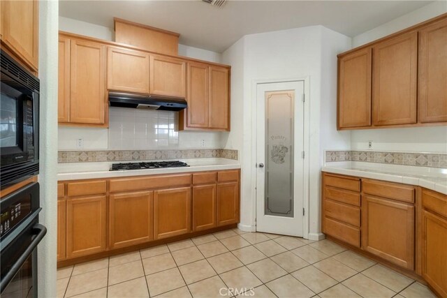 6631 Aggies Ct, Winton, CA 95388 - kitchen with black appliances, under cabinet range hood, tasteful backsplash, light tile patterned flooring, and tile counters
