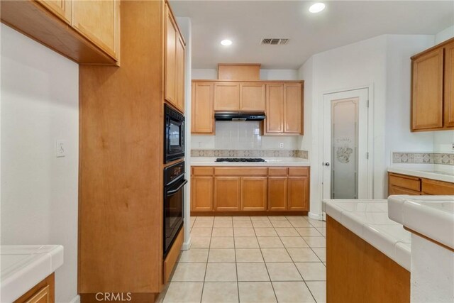 6631 Aggies Ct, Winton, CA 95388 - kitchen with black appliances, decorative backsplash, under cabinet range hood, light tile patterned floors, and tile counters