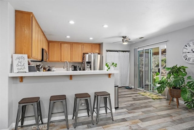 23317 Badger Creek Ln, Menifee, CA 92587 - kitchen with appliances with stainless steel finishes, tile countertops, a peninsula, ceiling fan, and a breakfast bar area
