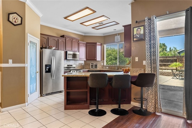 2802 Silver Shore Ln, Bakersfield, CA 93313 - kitchen featuring stainless steel appliances, a peninsula, backsplash, crown molding, and a breakfast bar area